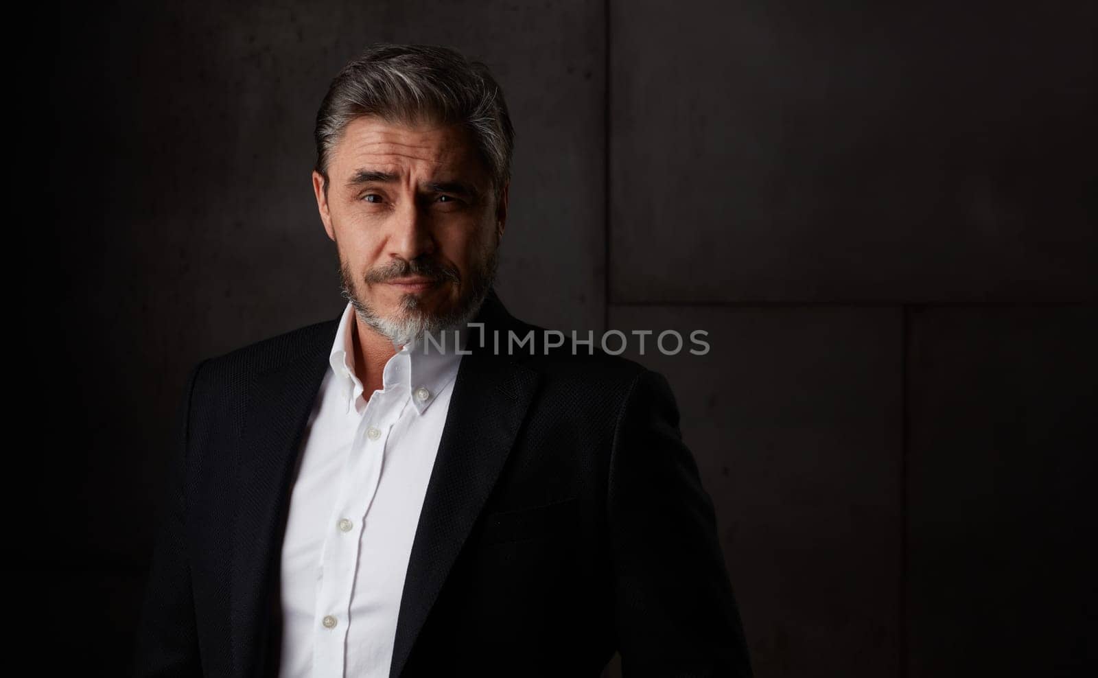 Business portrait of older man in 50s with gray hair against dark background. Businessman, copy space.