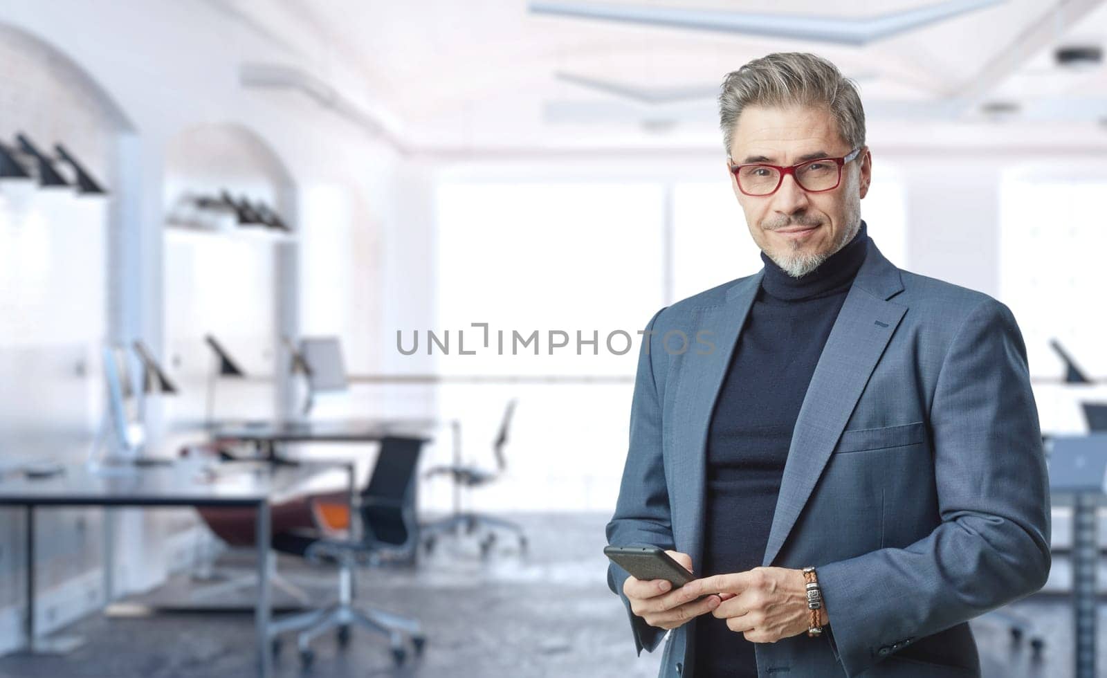 Business portrait - confident businessman in office. Trustworthy older man in his 50s with gray hair wearing glasses and jacket. Copy space.