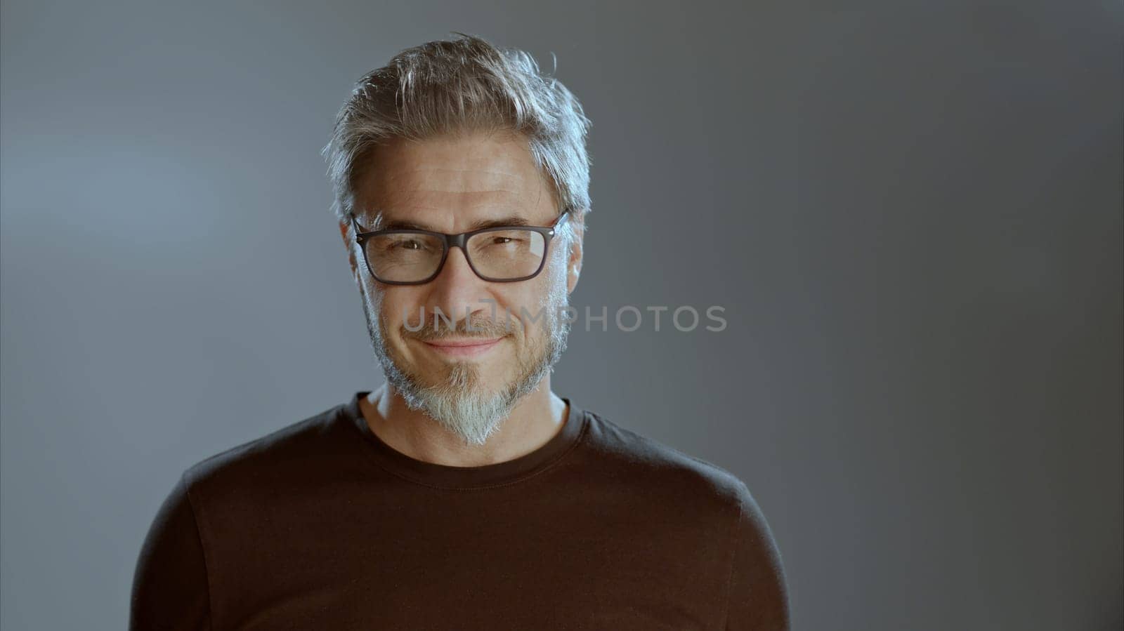 Portrait of happy older white man in glasses on gray background, smiling, copy space.