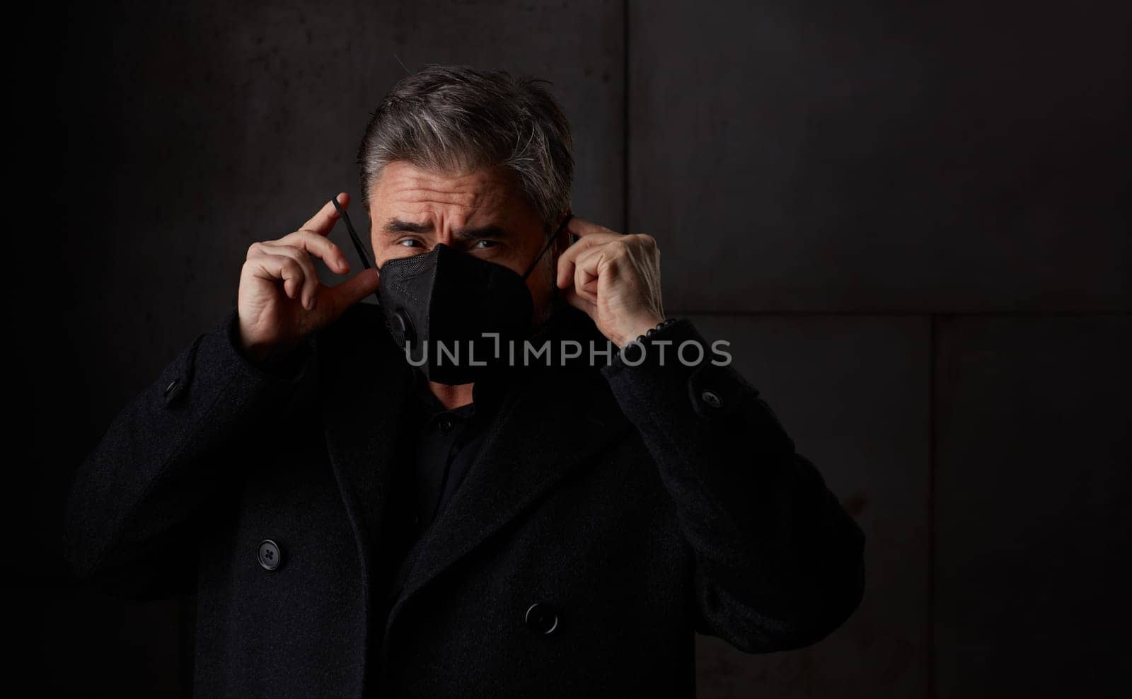 Covid-19 - portrait of older man in 50s with gray hair wearing medical face mask. Dark background copy space.
