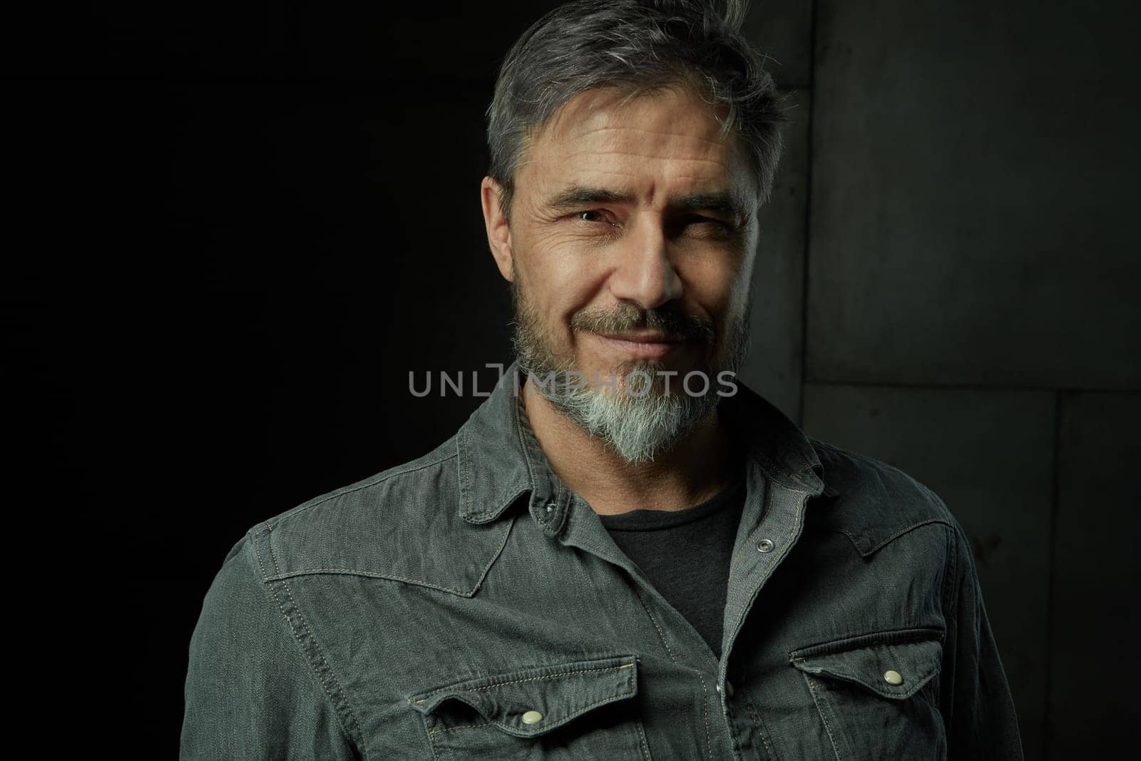 Portrait of casual older man with beard against dark background.