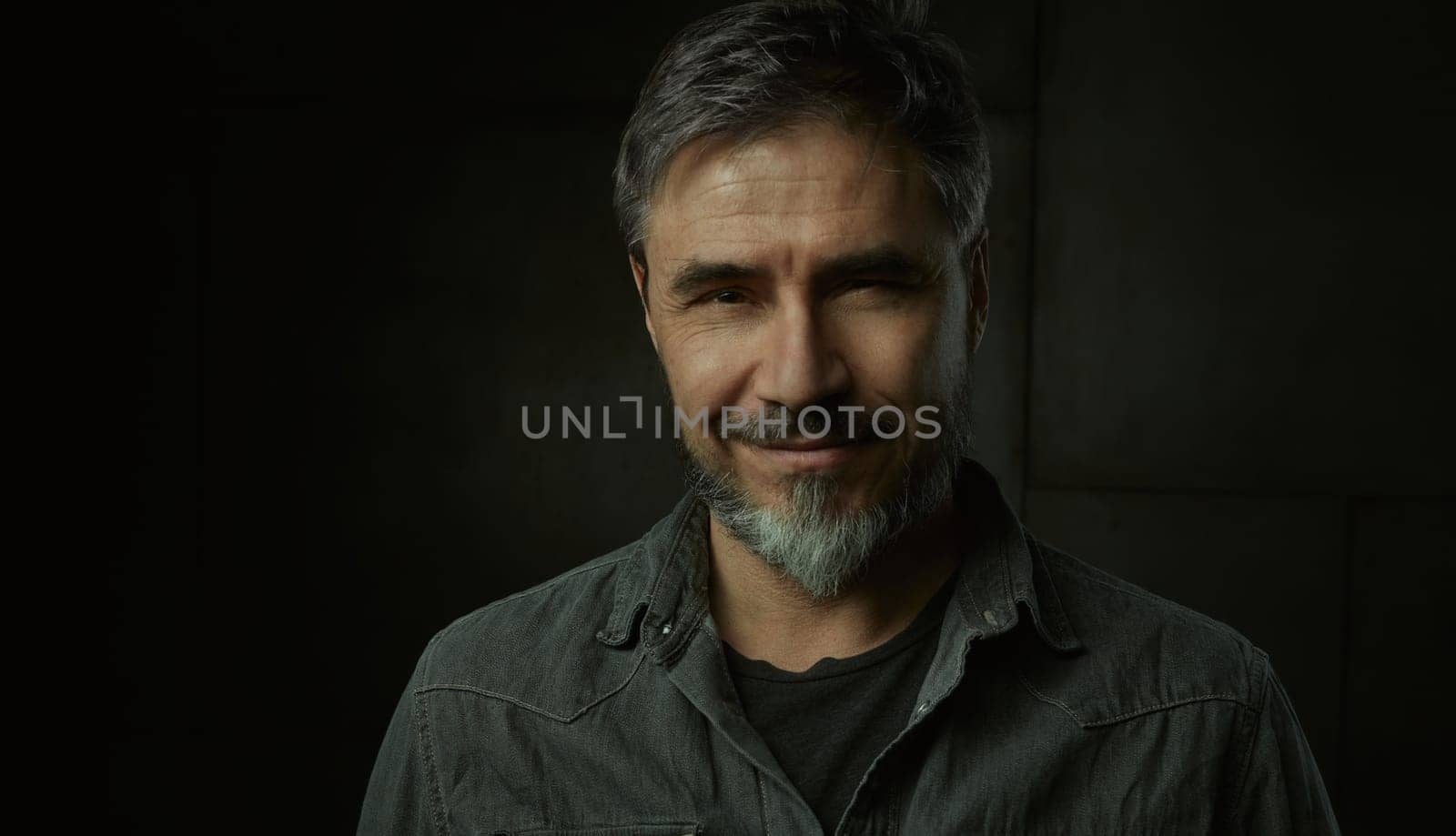 Portrait of casual older man with beard against dark background.