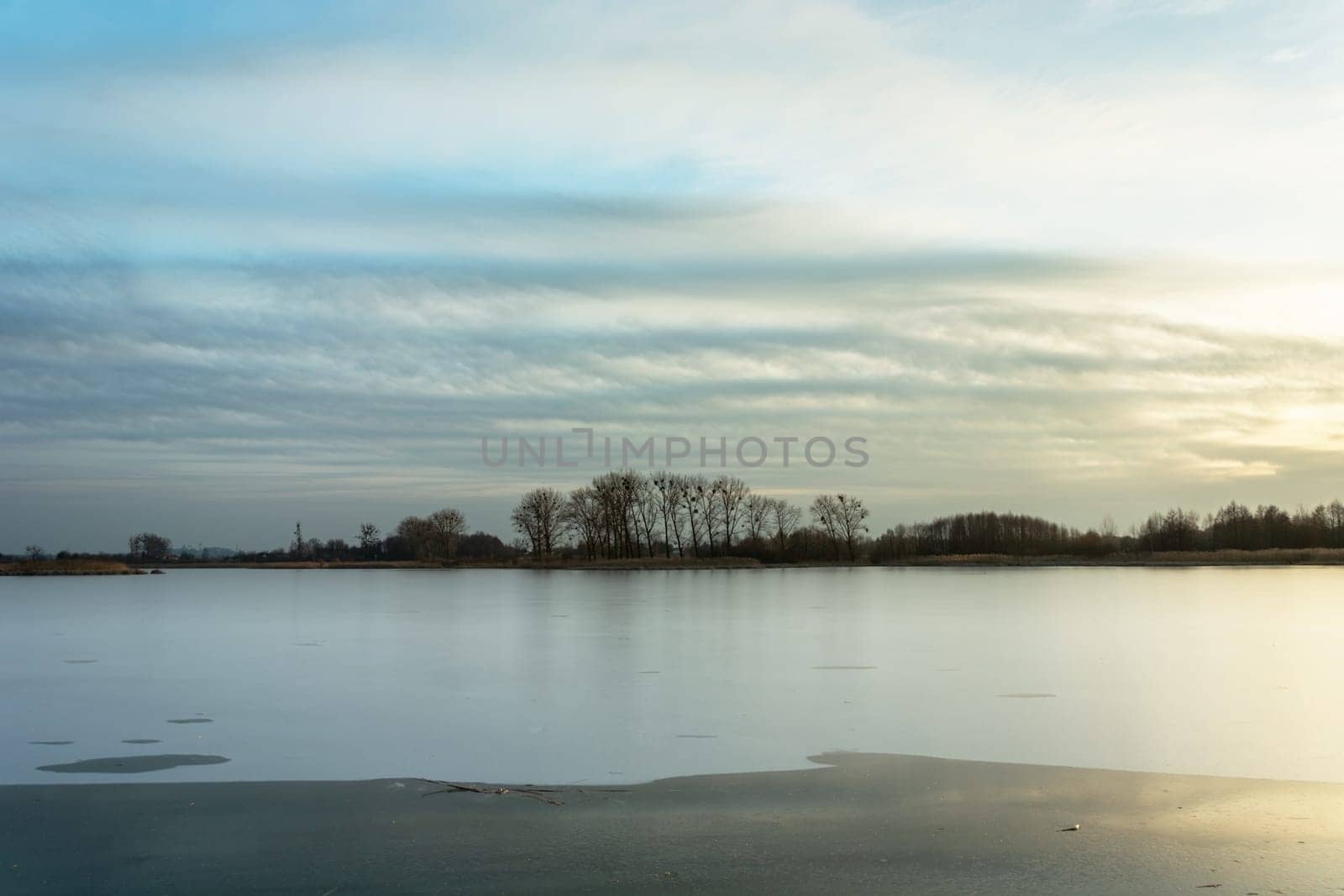 Frozen lake, trees on the shore and clouds, Stankow, Poland