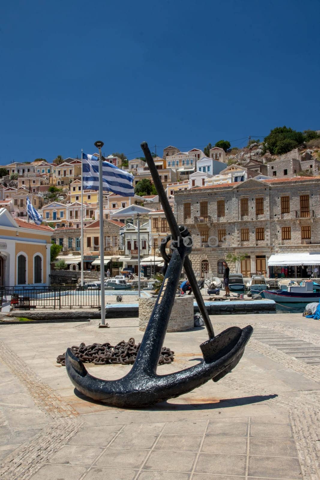 SYMI, Greece - 03 JUNE 2021. A old big Anchor sculpture on Symi town promenade on the pictorial port of Symi island in Greece. Dodecanese.