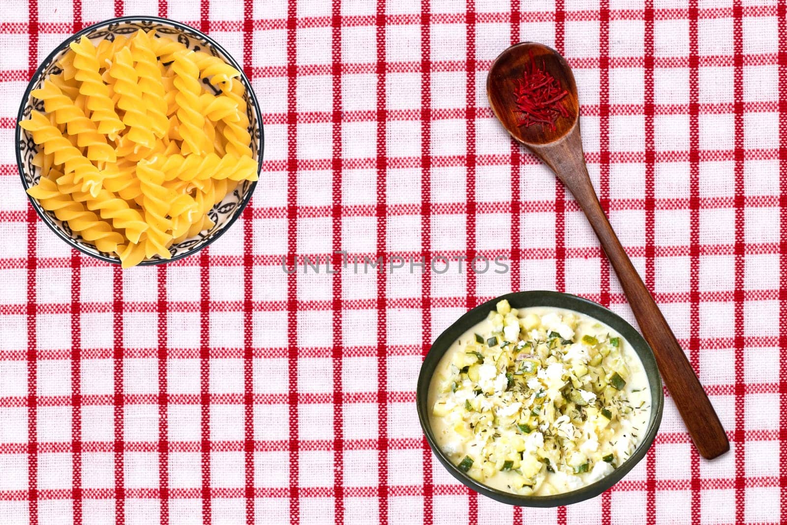 Vegetable food. Closeup of two bowls with noodles and greek soup and a spoon with safran spice threads on a tablecloth. Healthy eating and nutrition. Top view with space.