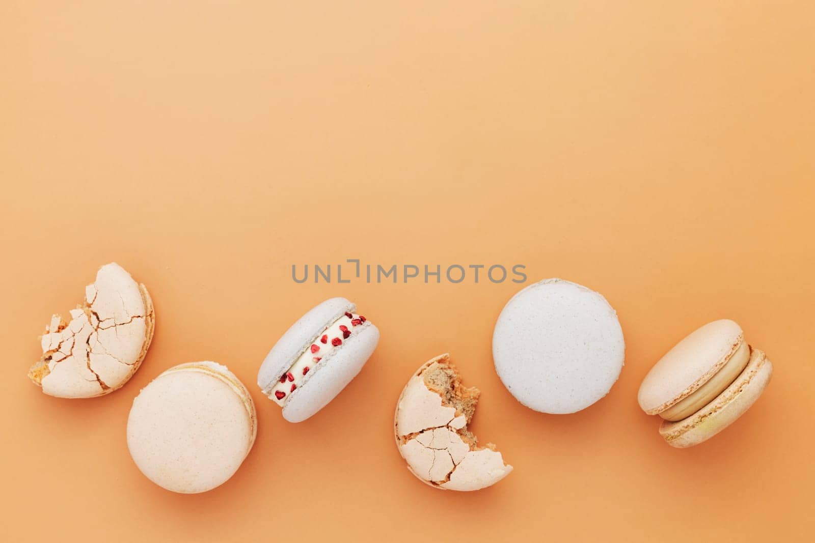 White, yellow, gold macaron cookies. Colorful, sweet small French macaroon cakes laying on the table. Light yellow-beige background. Broken cut, bitten parts, halves. High quality photo