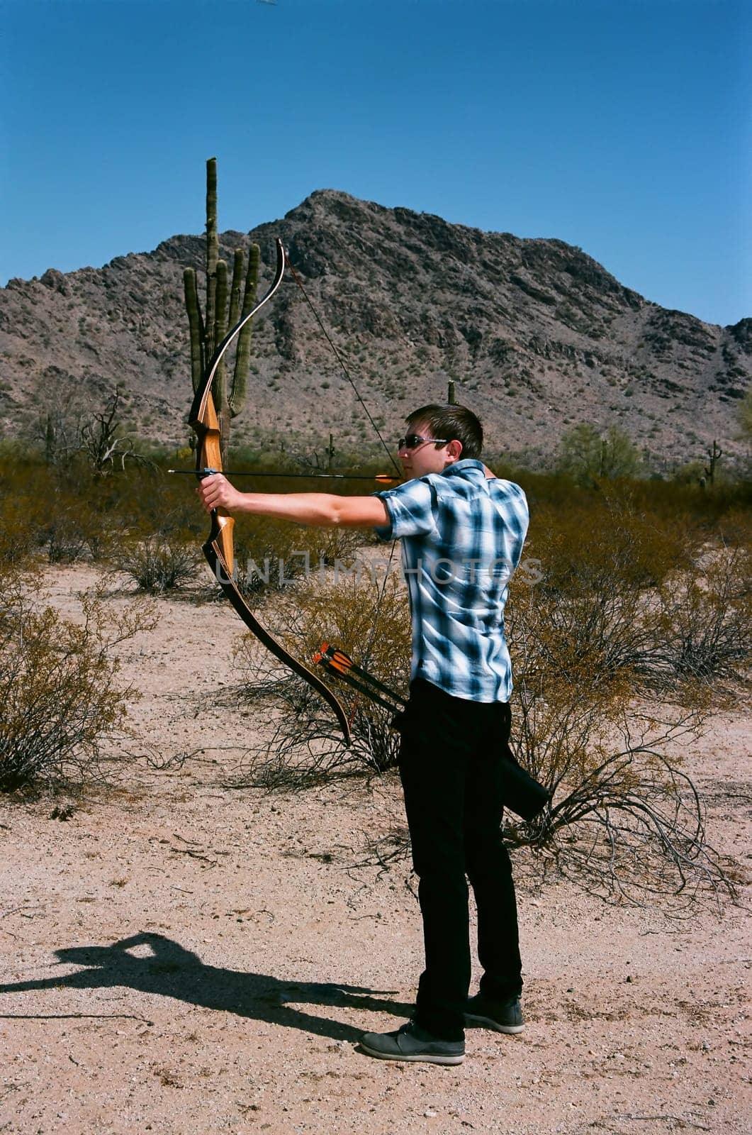 Young man shooting a bow and arrow in the desert