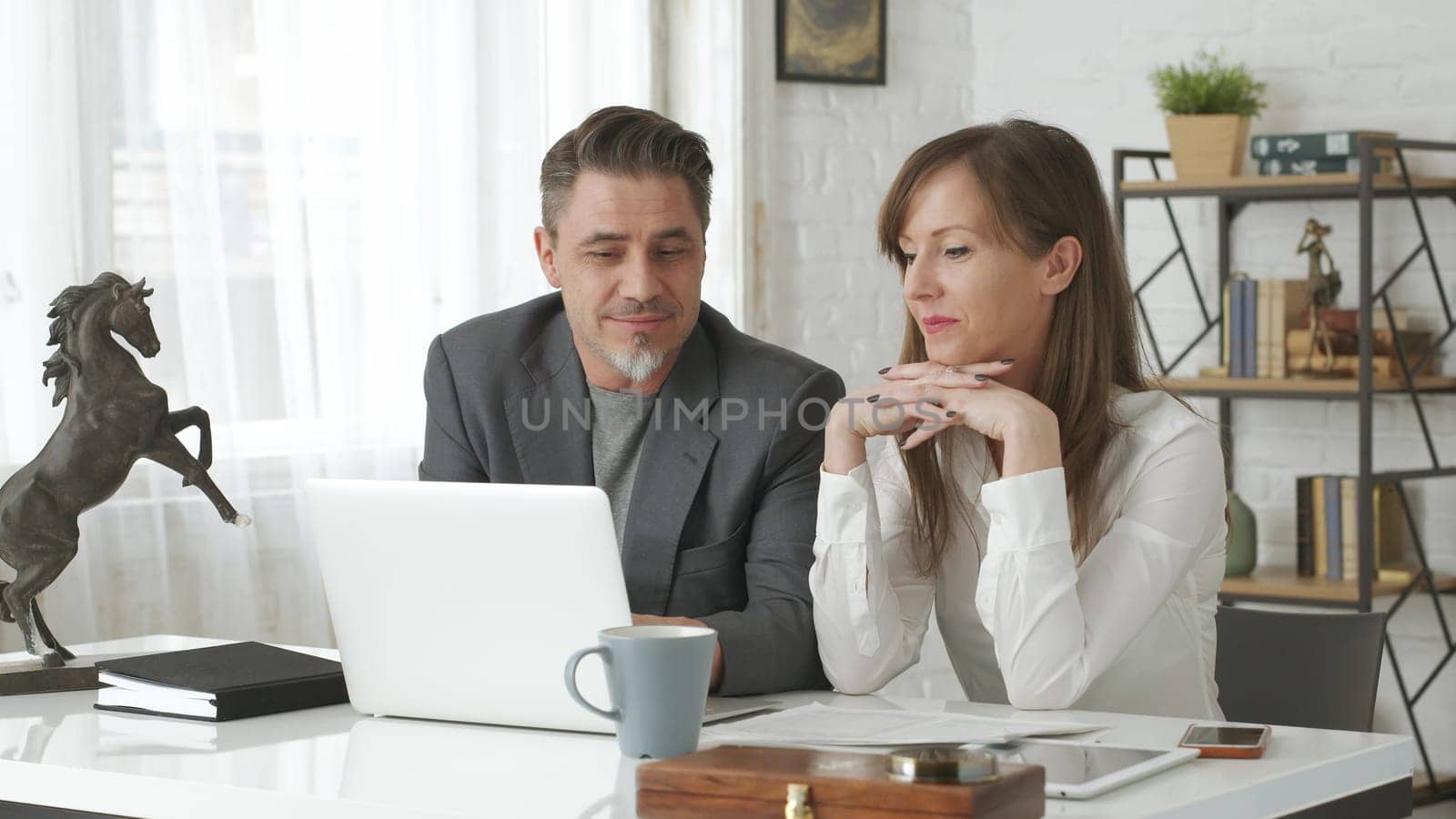 Happy business people working at desk using laptop computer, talking, working together