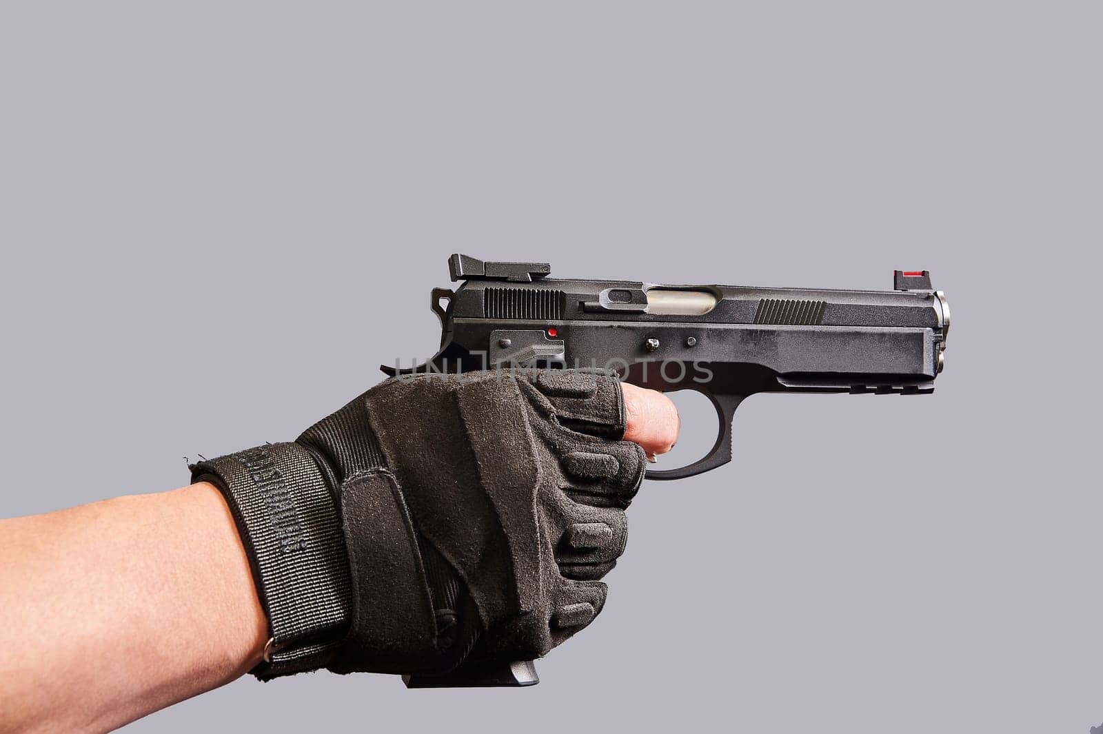 A man's hand holds a black pistol in his hand on a gray background. High quality photo