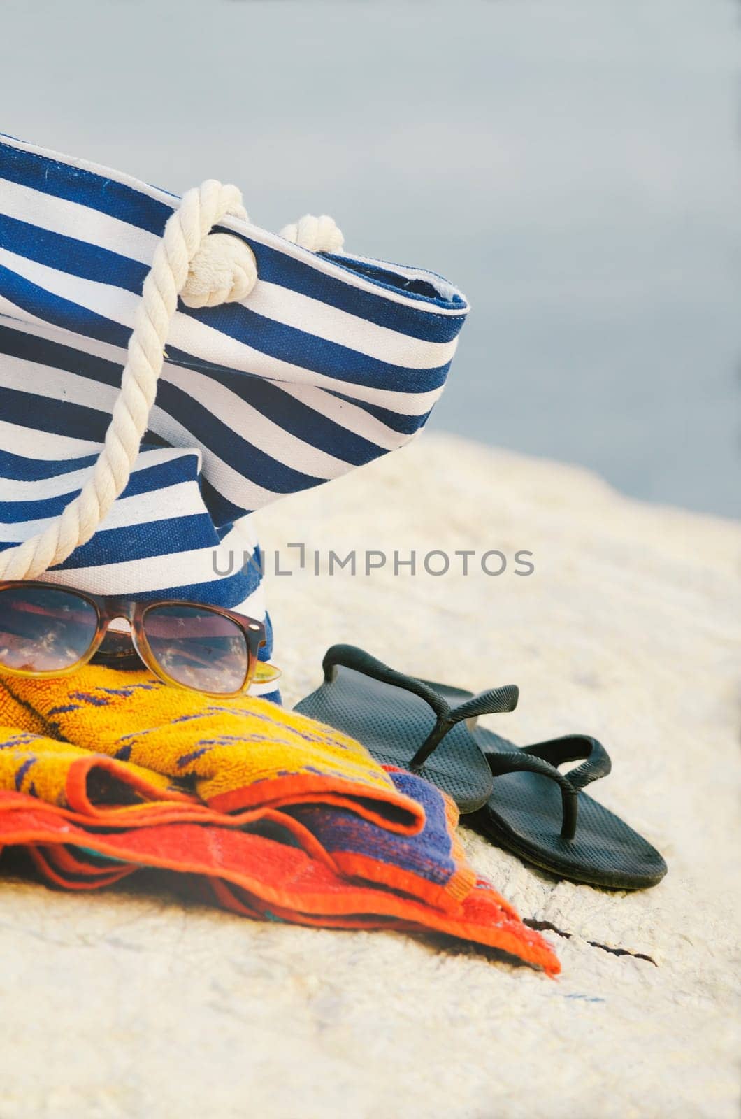 Sunglasses, towel, bag and flip-flops on the beach.