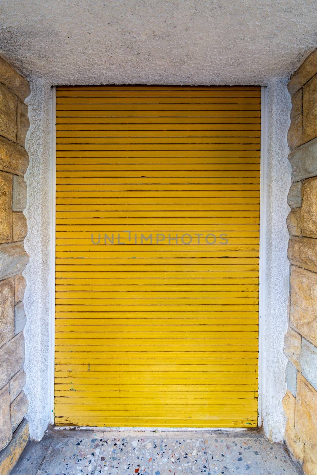 Background of bricks stone wall and closed yellow rolling shutter door