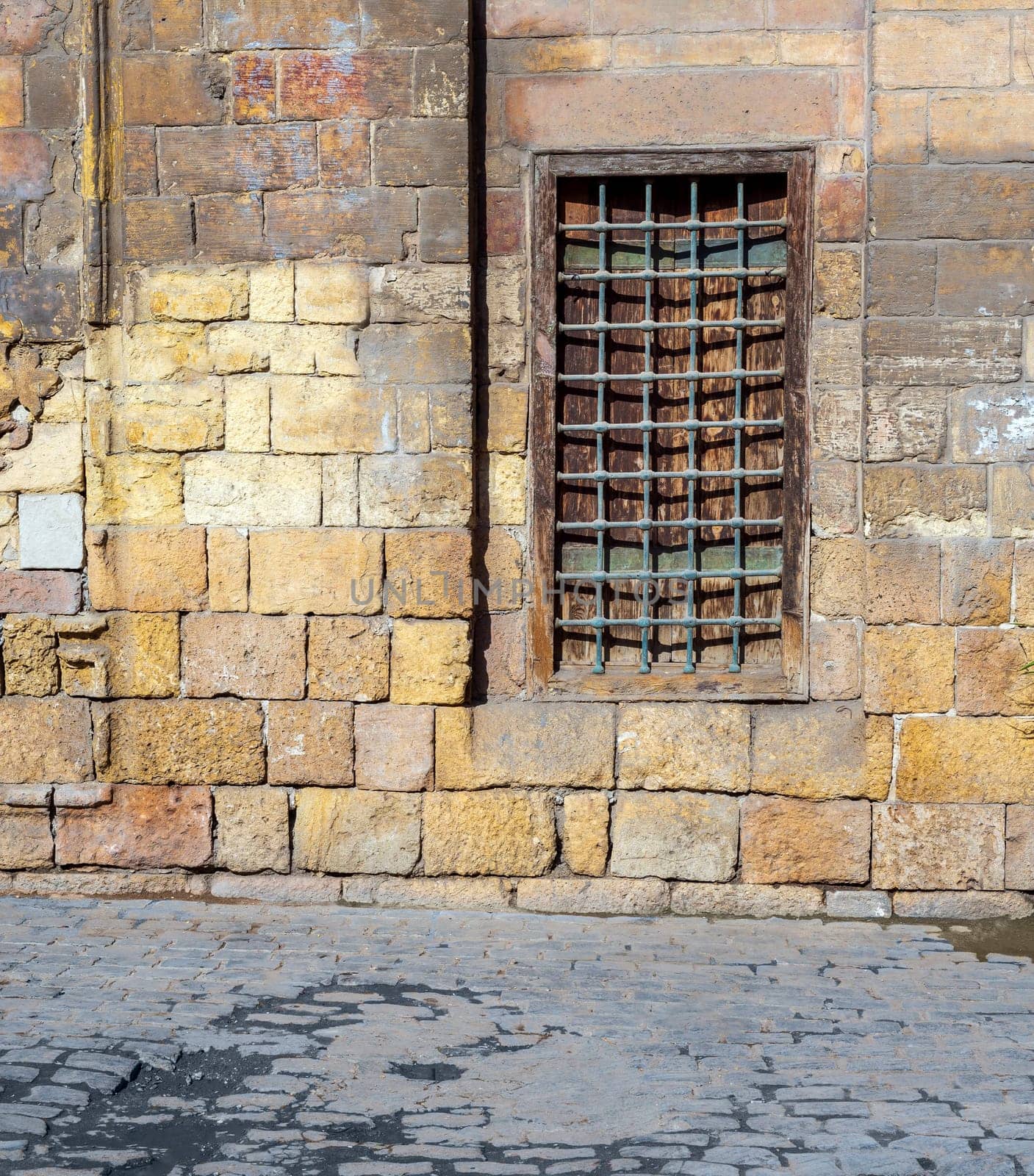 Daylight shot of grunge wooden window with decorated wrought iron grid over stone bricks wall and marble garden bench