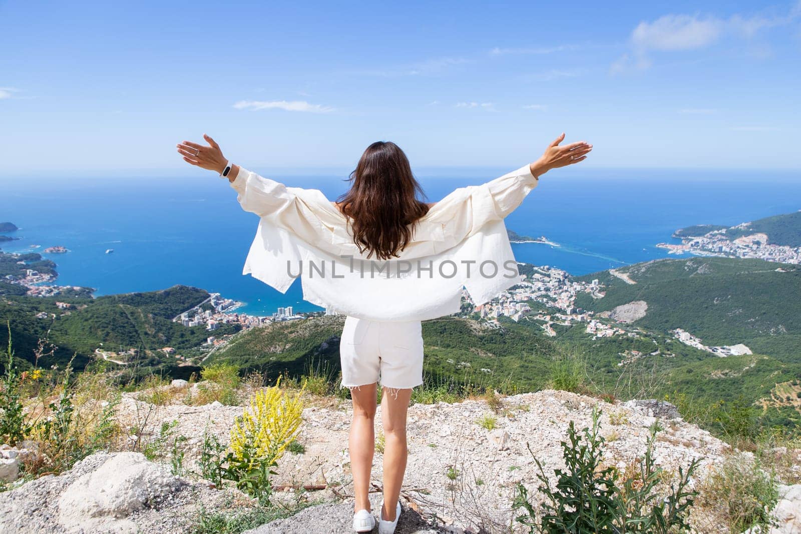 Young beautiful woman stands with her back and looks at the old town of Budva, Montenegro