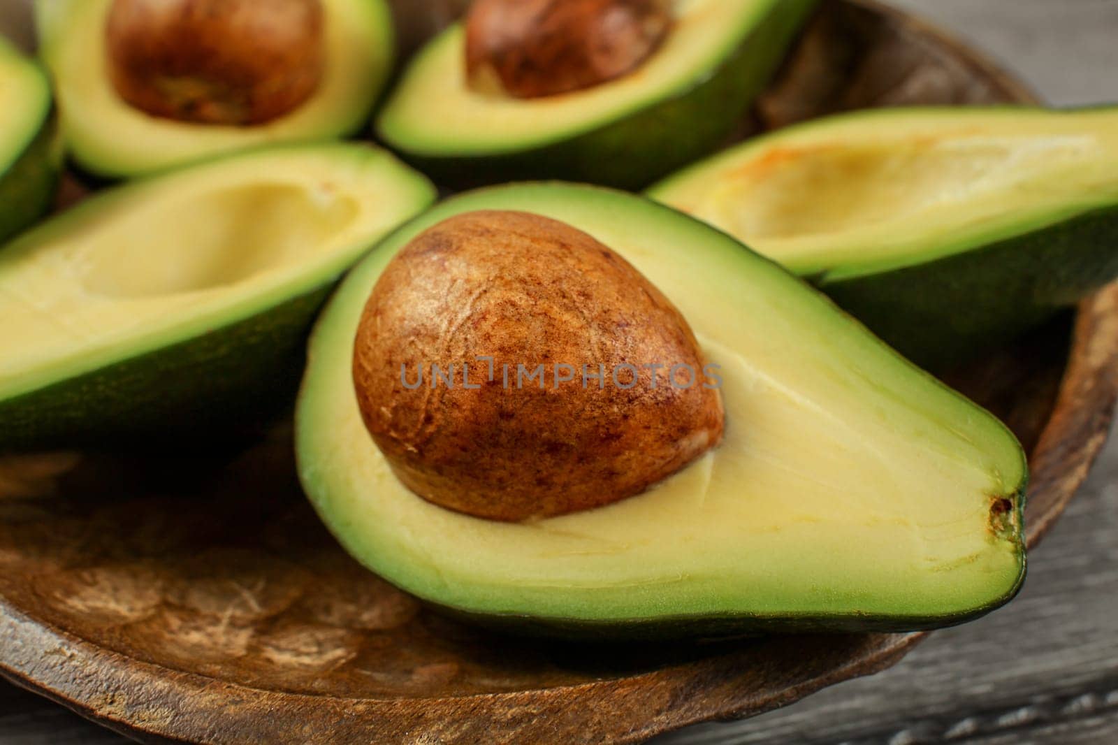 Close up photo of avocado halves on wooden carved bowl, detail on the brown seed / pit.