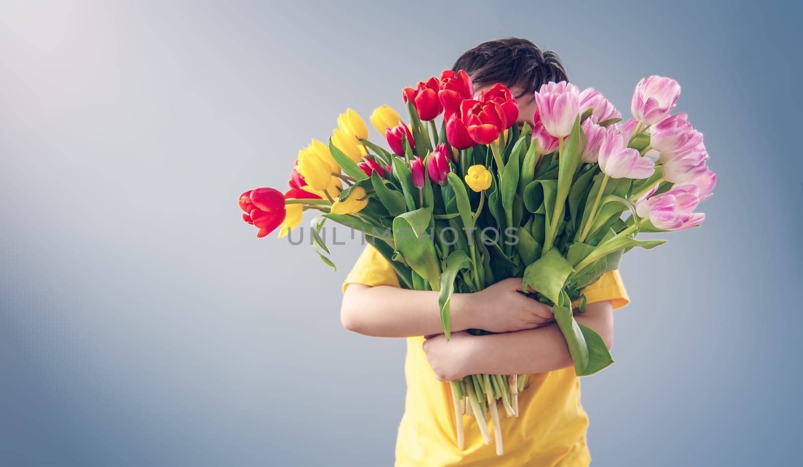 Cute boy standing indoors with bouquet of the colourful tulips. Concept of the Mother's day and family relationship.