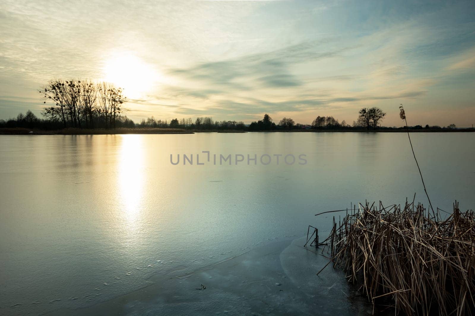 Beautiful sunset over a frozen lake with reeds, Stankow, Poland
