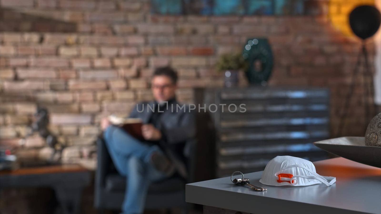 Covid-19 virus danger - Man staying in safety of home reading book leaving virus protective mask on desk.