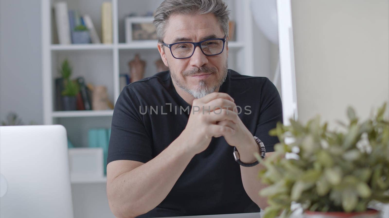 Portrait of happy older man in glasses sitting at desk working with laptop in home office. Confident 50s businessman in casual with gray hair smiling.