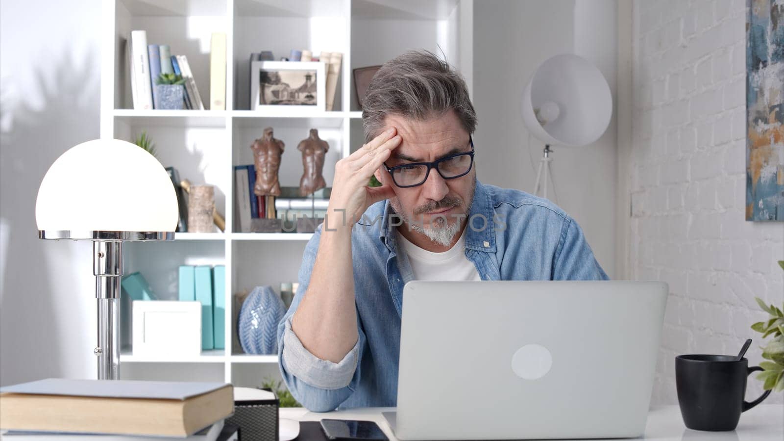 Older man working online with laptop computer at home sitting at desk. Home office, surfing internet, study room.
