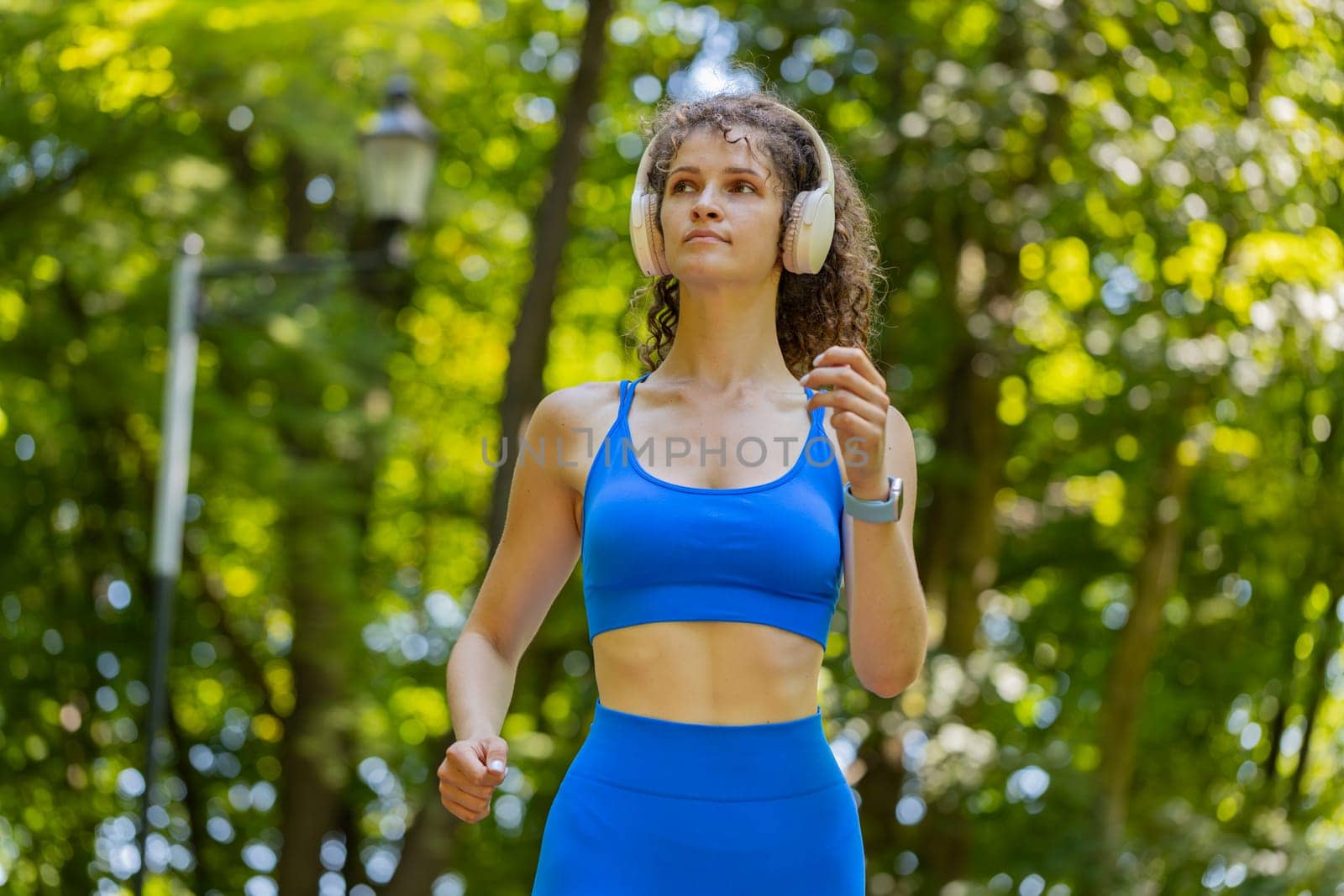 Active sportswoman jogging training marathon run, listening to music in wireless headphones. Workout cardio outside in park at morning. Young girl enjoying healthy lifestyle. Female athlete jogger.