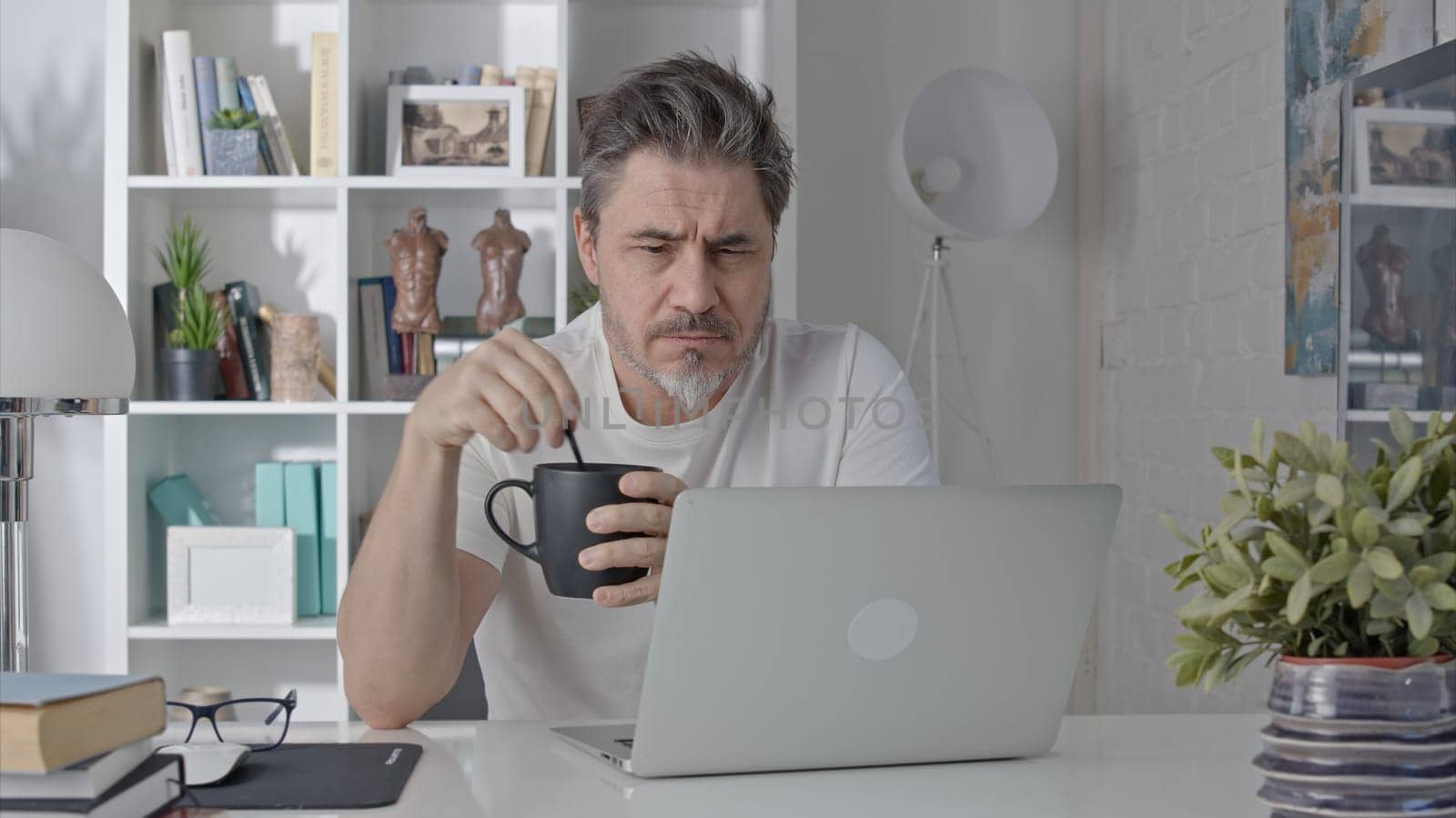 Older man working online with laptop computer at home sitting at desk. Home office, browsing internet, study room.