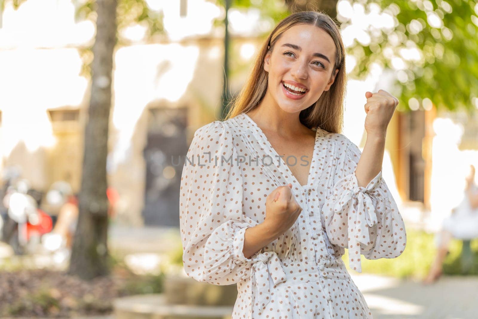 Excited happy woman traveler shouting, celebrating success, winning, goal achievement, good news, lottery jackpot luck, victory outdoors. Young lady standing on urban city sunshine street. Lifestyles