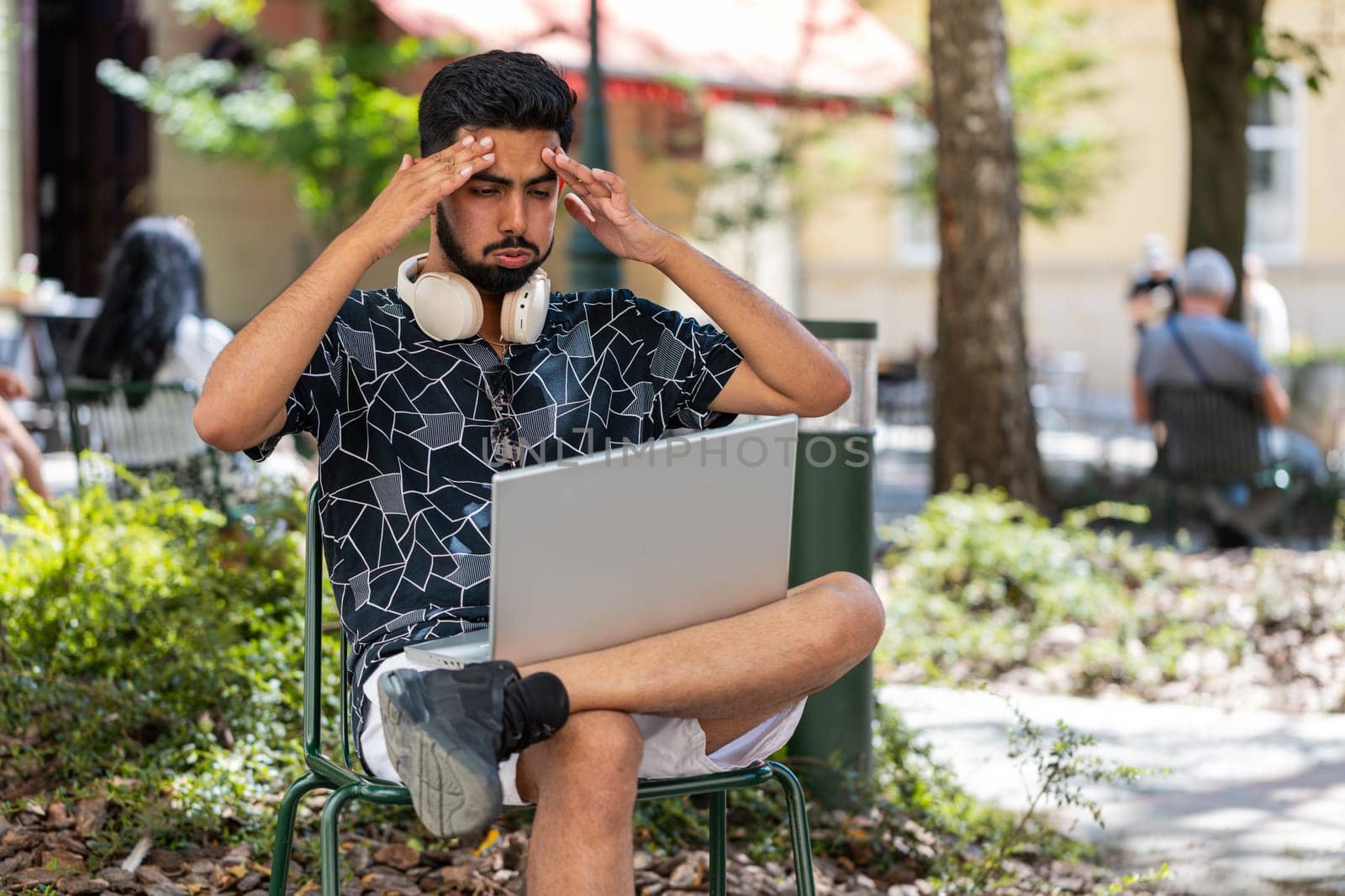 Hispanic young man using laptop computer typing browsing, loses becoming surprised sudden lottery results, bad news, fortune loss, fail. Guy sits in urban city street park outdoors. Town lifestyles.