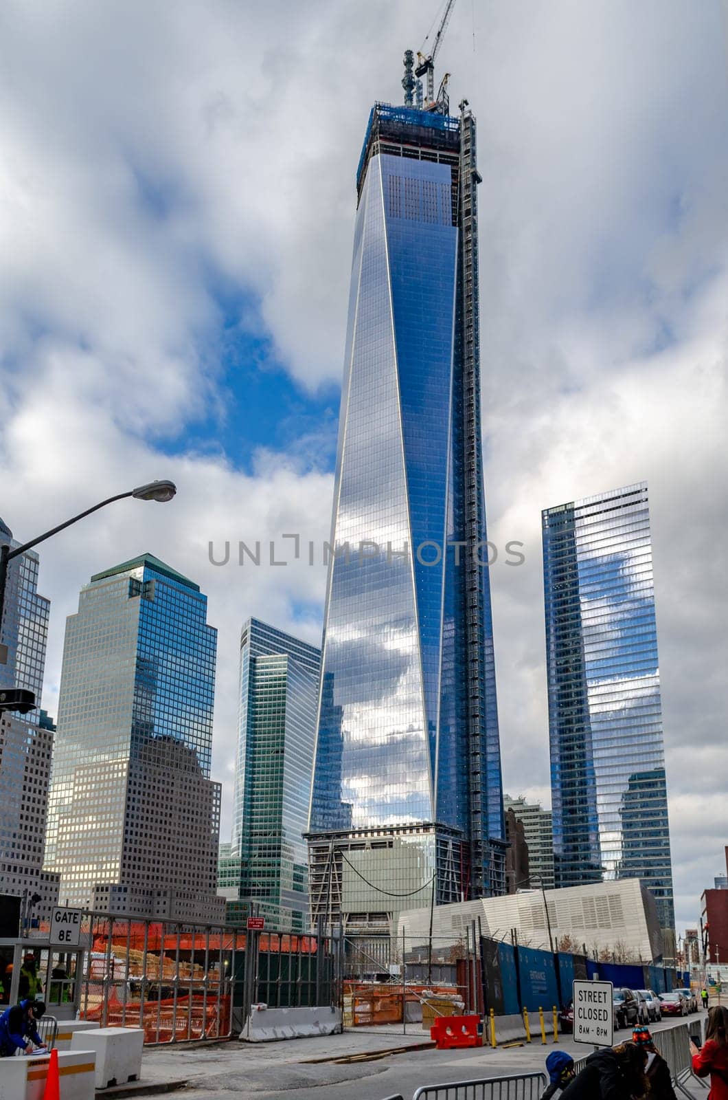 One World Trade Center construction area with  clouds reflection in the window, crane on top during daytime with overcast, New York City, view from low angle, vertical