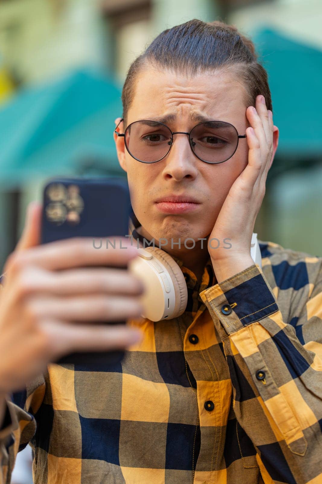Shocked young man using smartphone typing browsing, loses becoming surprised sudden lottery results, bad news, fortune loss, fail. Tourist guy standing in urban city street outdoors. Town lifestyles.