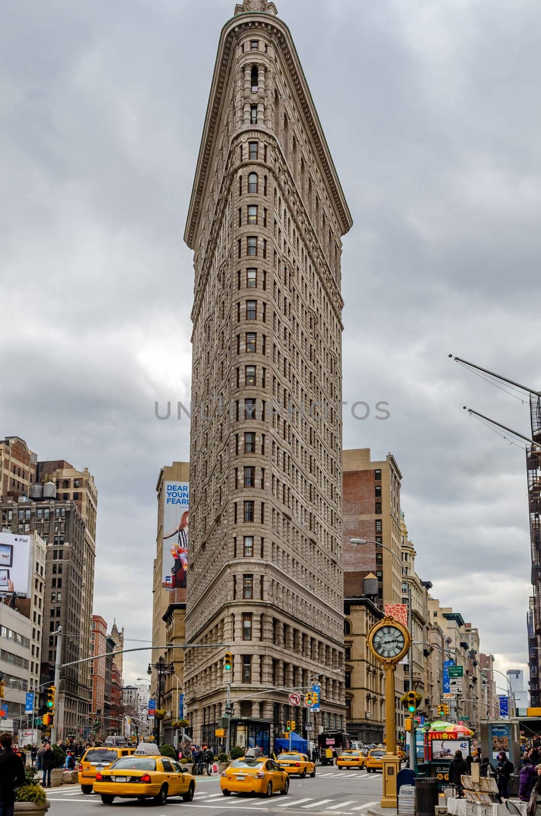 Flatiron Building New York City with street and crosswalks, yellow taxi cabs in forefront during daytime with overcast, view from low angle, vertical