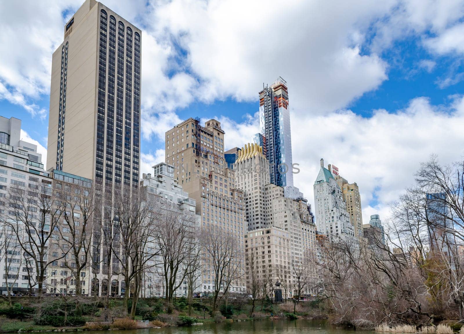 Skyline of Manhattan with Essex House and other Skyscraper, The Pond at Central Park Lake in forefront, view from low angle, cloudy sky during winter, horizontal