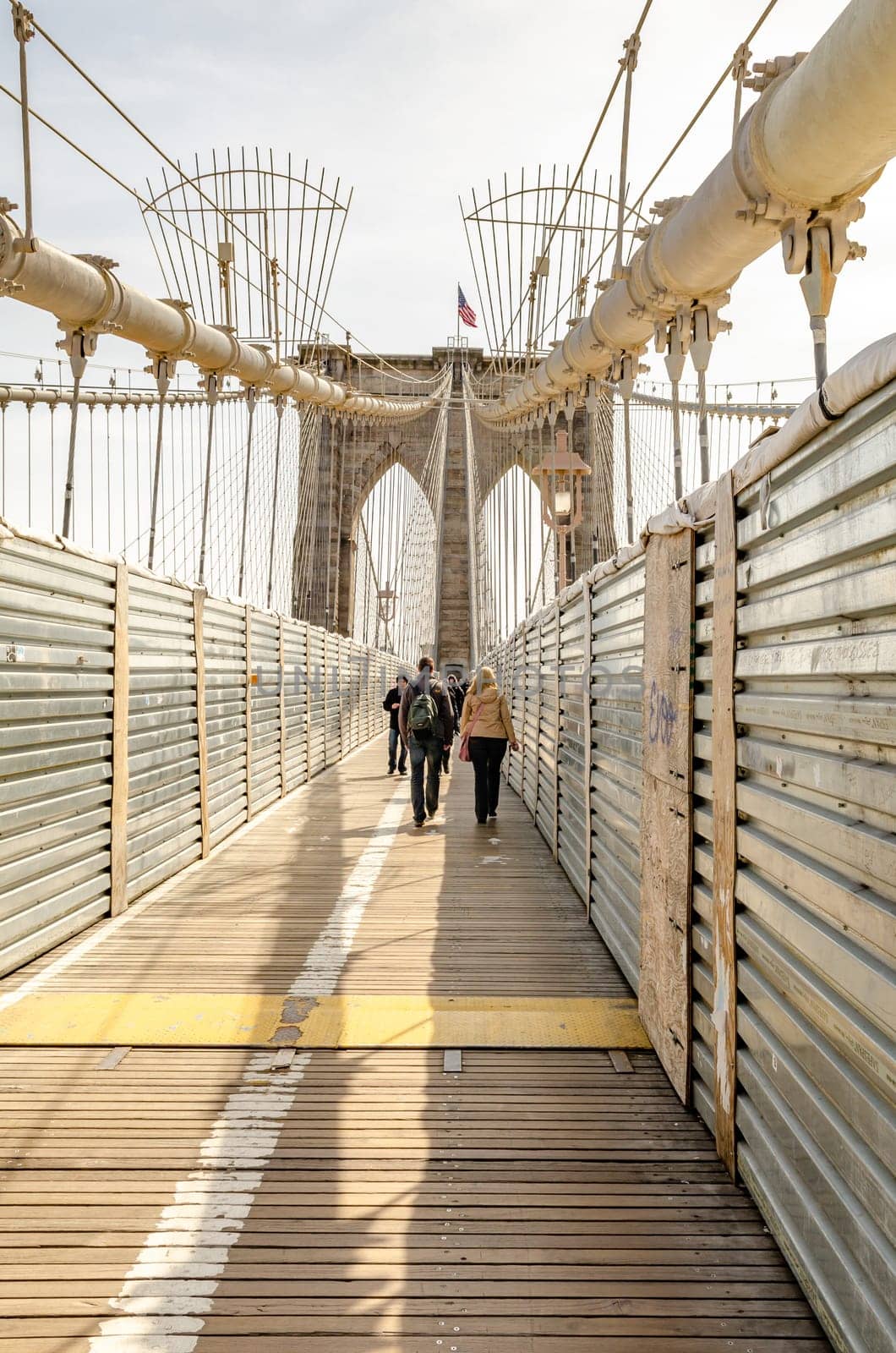 People walking on Brooklyn Bridge during sunset, New York City, rear view, construction area on the bridge, vertical