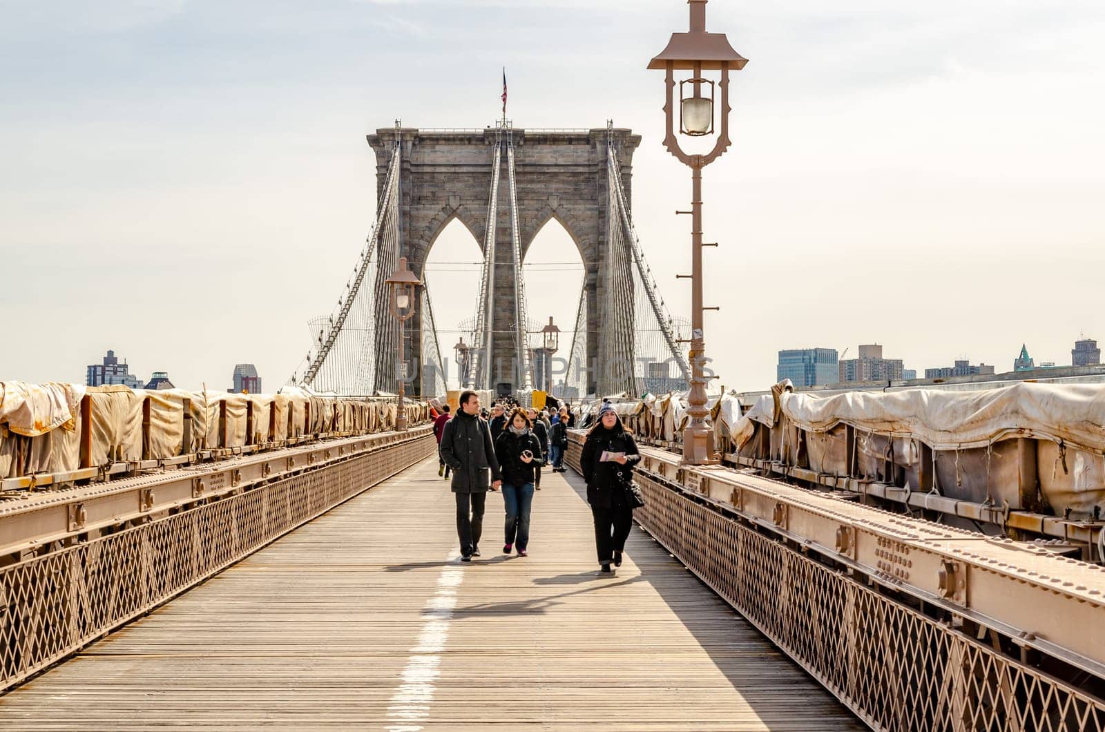 People walking on Brooklyn Bridge, New York City in the evening, street lamp in forefront, clear sky, construction area on the bridge, horizontal