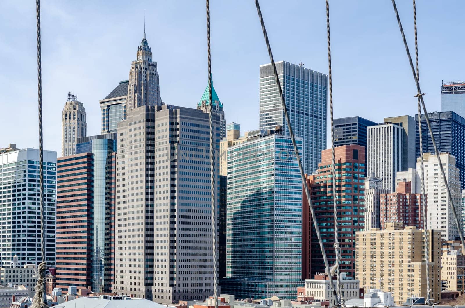 Skyline of Manhattan during daytime with clear sky with wire ropes of Brooklyn Bridge in the forefront, horizontal