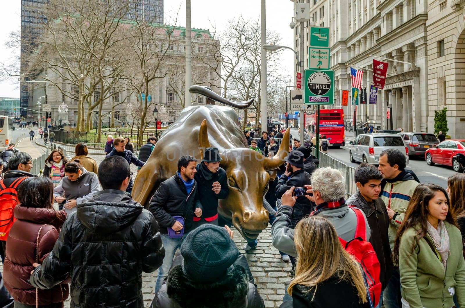 Bull and Bear, Bull Statue Monument at New York Stock exchange with lots of tourist in the forefront taking photos, during winter, horizontal