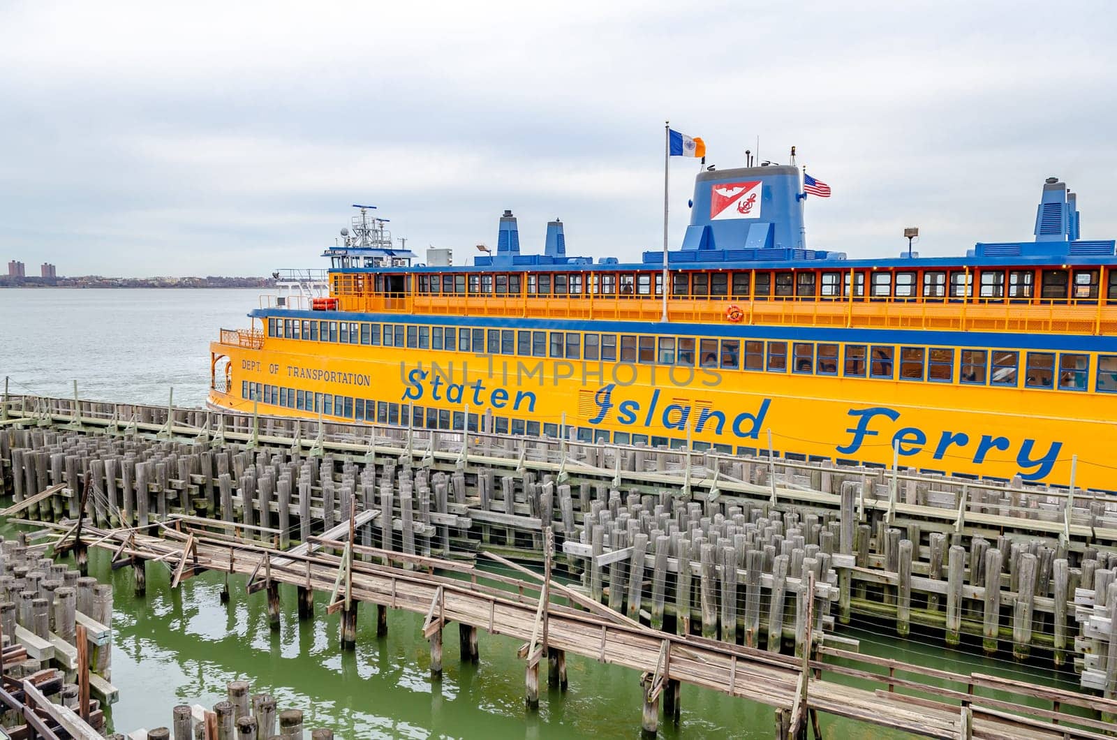 Yellow Staten Island Ferry at the Staten Island Terminal, wood jetty in the forefront, side view, during winter day with overcast, horizontal