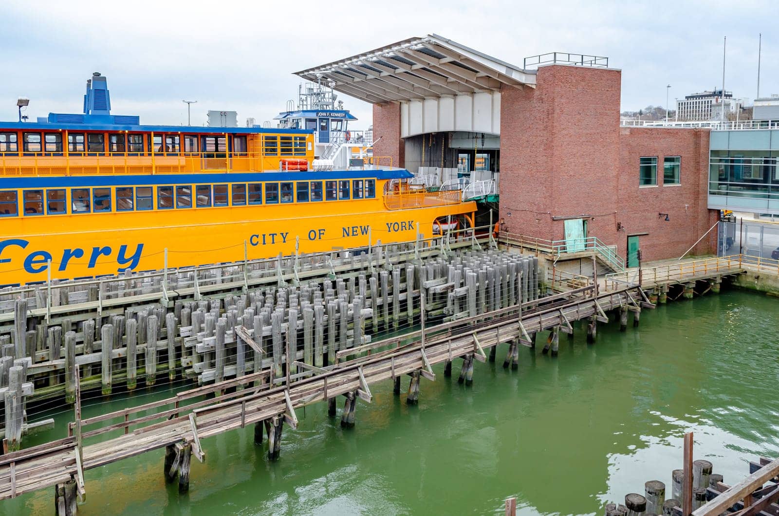 Yellow Staten Island Ferry at Staten Island Terminal, side view, wood jetty in the forefront, during winter day with overcast, horizontal