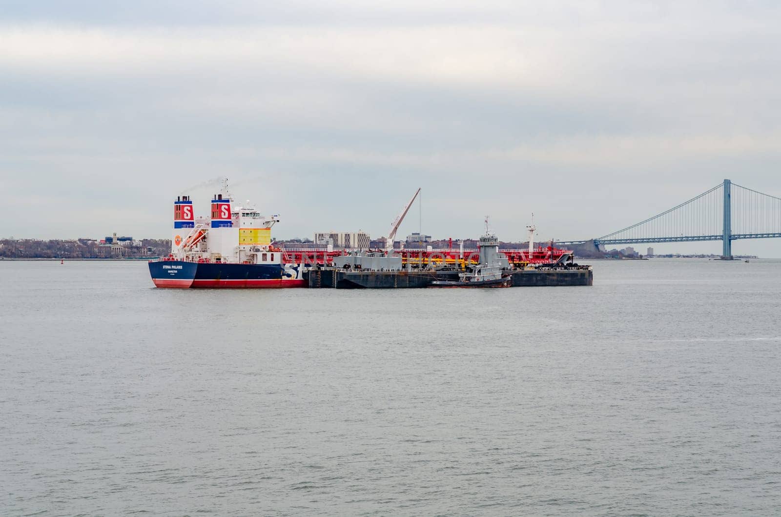 Different industrial ships, Stena Polaris Hamilton at Hudson River, New York City, during winter evening with overcast, Verrazano-Narrows Bridge in the background, horizontal