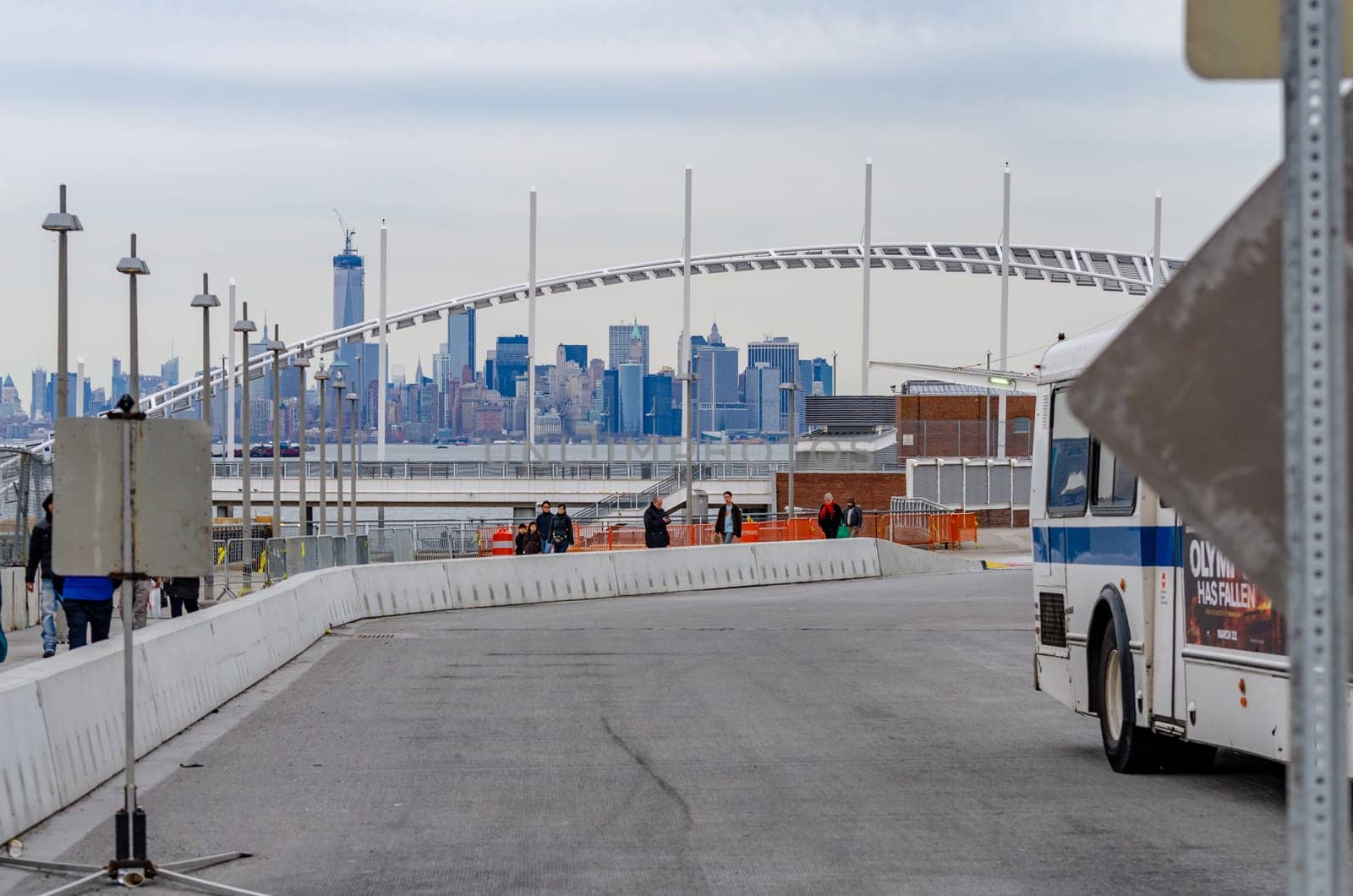Staten Island Ferry Terminal People walking in line to exit the Terminal, Skyline of Manhattan, New York City in the distance, bus passing by, during winter day with overcast, horizontal
