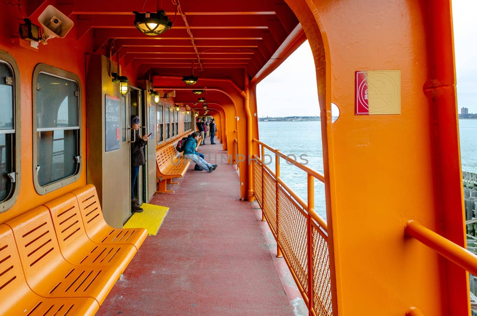 People waiting on Staten Island Ferry for the ferry to leave Staten Island, standing, sitting on benches, indoors New York City, during winter day with overcast, horizontal