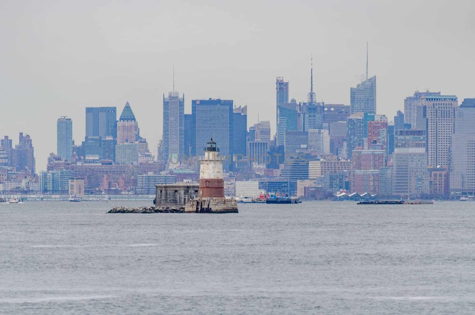 Old brown white Lighthouse at Hudson river in front of Manhattan, New York City, during winter day with overcast, view from the distance from Staten island, horizontal