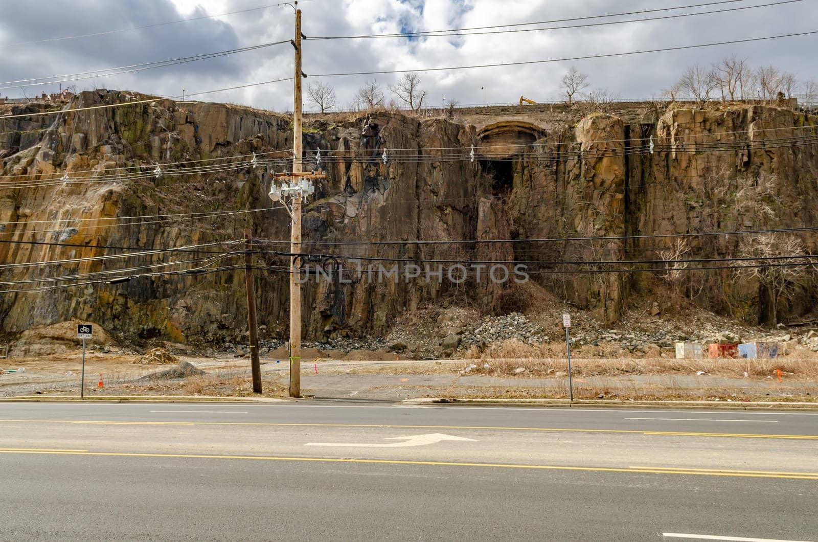 Rock with old wooden electric power pole and road in the forefront, North Bergen, New Jersey, during a sunny winter day, horizontal