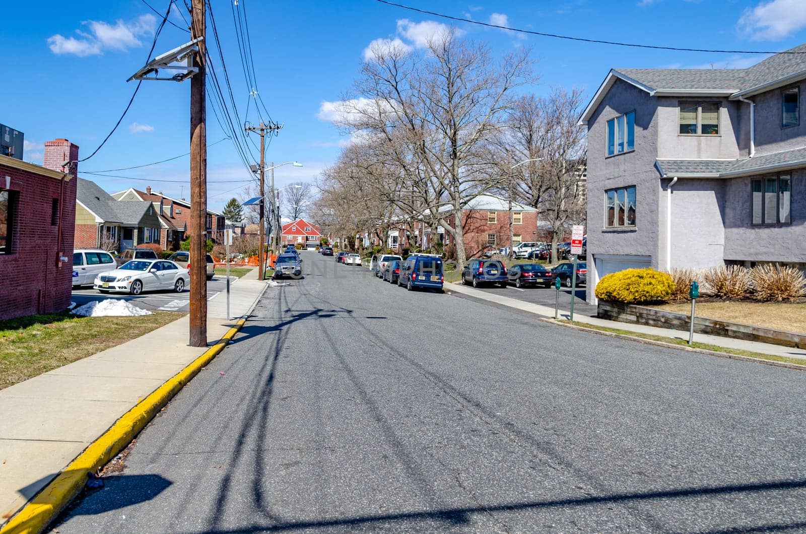 Typical Street in New Jersey with parked cars next to the sidewalk, residential area, during a sunny winter day, power pole at the street, horizontal