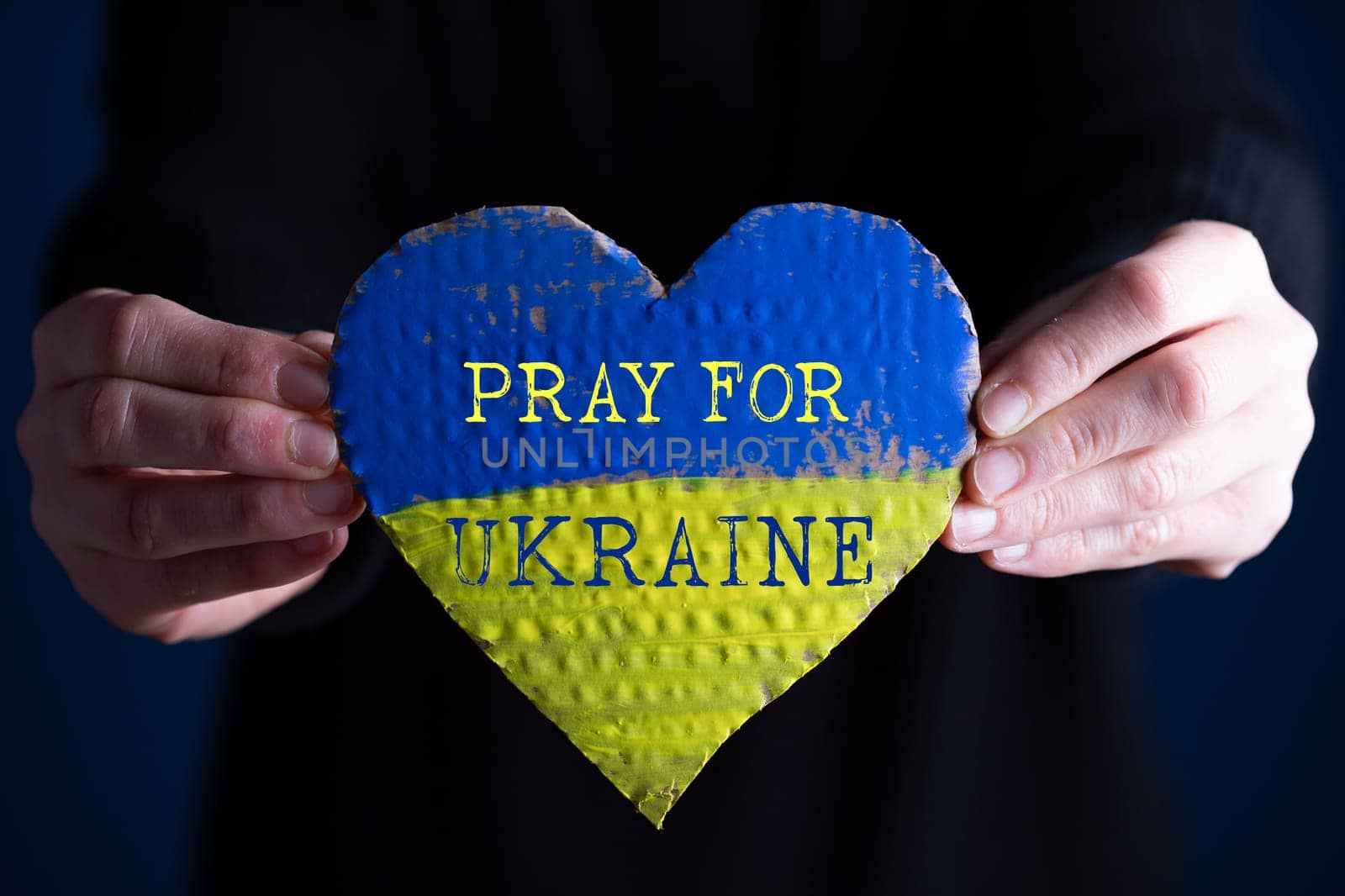 Heart shaped flag of Ukraine in female hands, Pray for Ukraine text.  The concept of solidarity with the citizens of Ukraine.