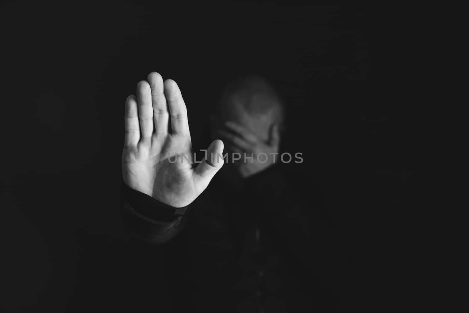 Sad, angry man showing stop sign on dark background. Low key photo.