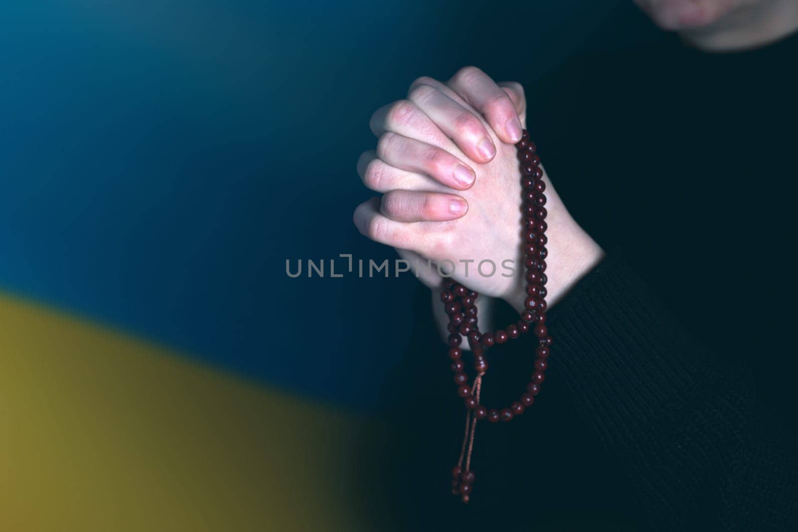 Sad woman with Ukraine flag at background praying. Concept of standing with Ukrainian nation in war with Russia.