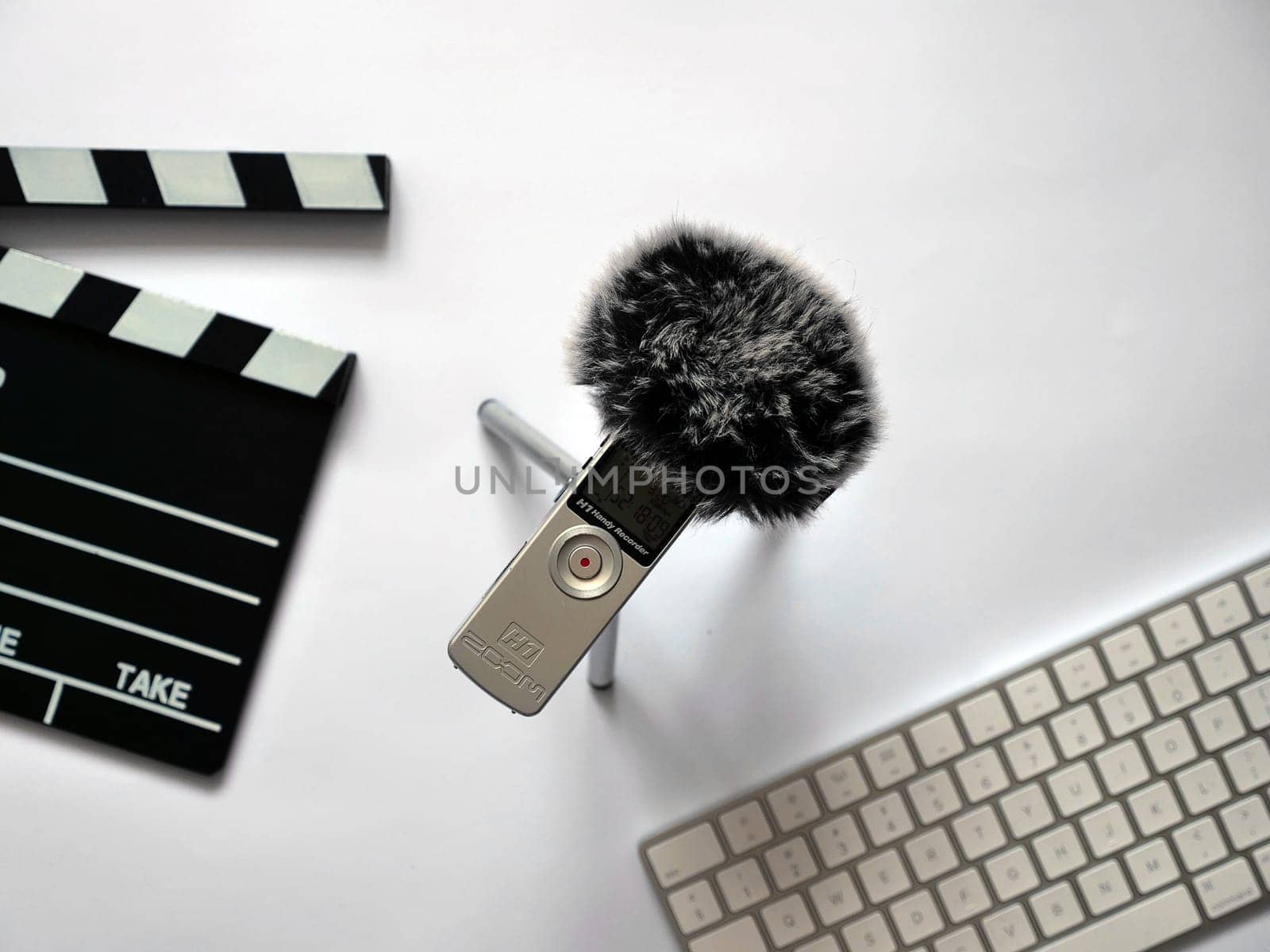 Record audio inside on zoom h1 recorder with dead cat in recording studio on white background in natural daylight. The background shows objects such as Clapperboard and keyboard. You can use this photo in any project related to sound recording, podcast, recording studio, interview or journalistic activity.. High quality photo