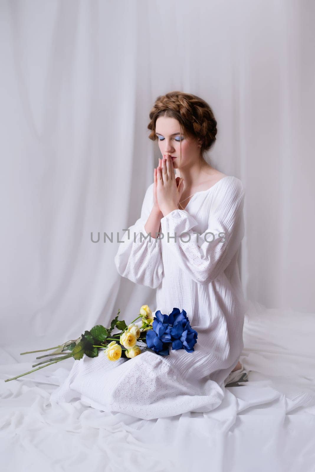 Beautiful Ukrainian girl in a white dress and flowers prays for ukraine during the war on white background . Symbol of the yellow blue flag. The calm lady. Peace in World