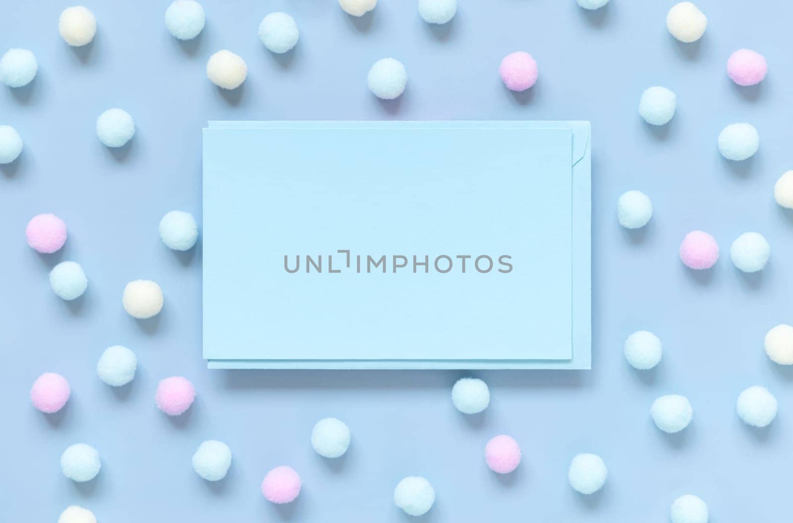 Blank card between pastel pom-poms on light blue top view. Romantic scene with blank horizontal card with place for text flat lay. Spring or boyish concept