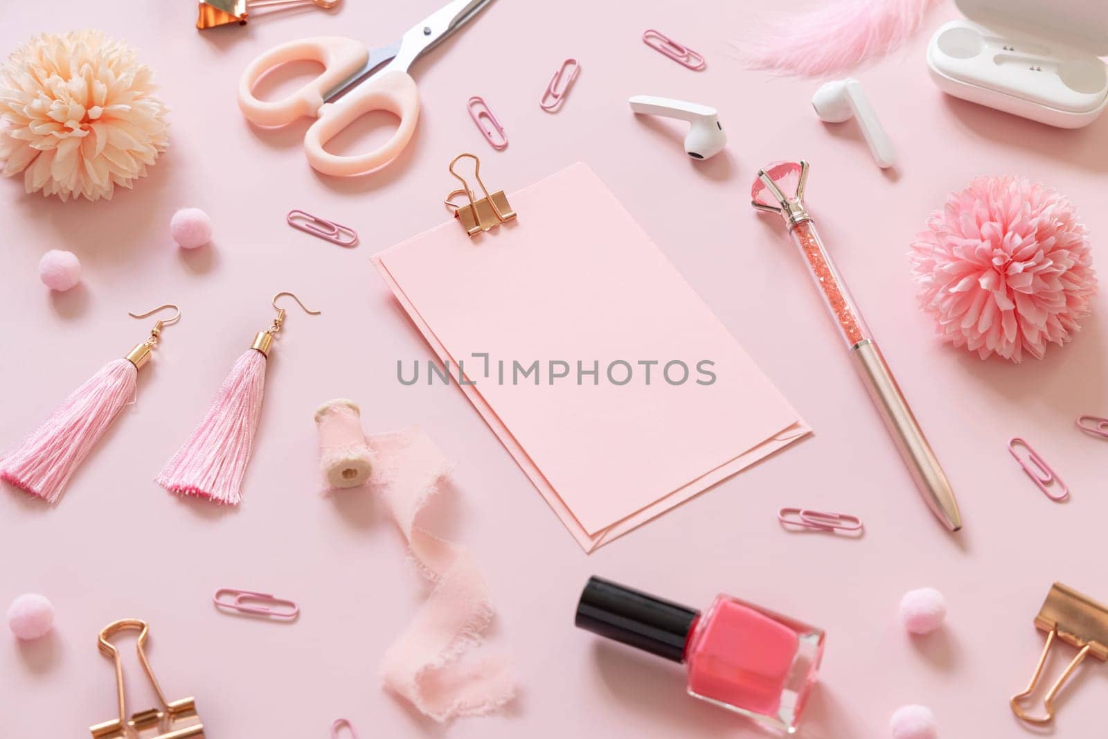 Paper with a clip and Pink school accessories on pastel pink, close up, textbook mockup. Girly workplace with scissors, pencils, pen, paperclips, earrings and watch. Back to school concept